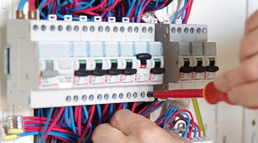 Vue des mains d'un électricien en train de câbler un tableau {{brizy_dc_image_alt imageSrc=